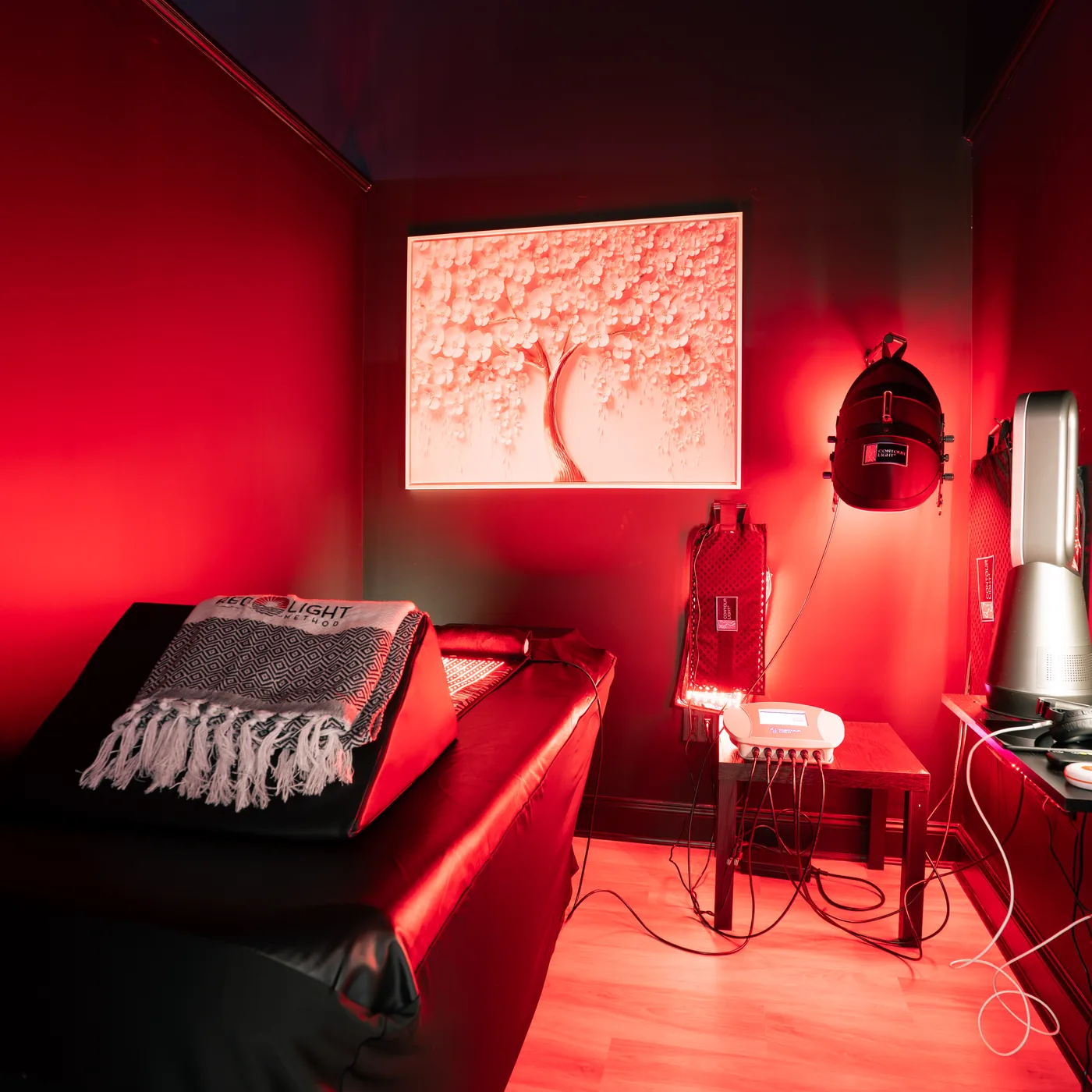 A treatment room bathed in deep red light, with a bed, a wall-mounted light array and a framed cherry blossom lightbox